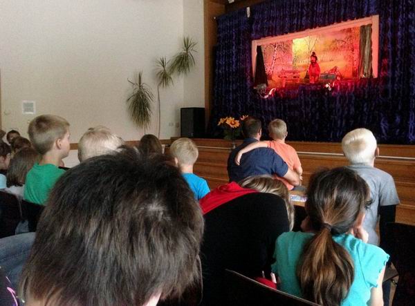 Kinder gucken dem Marionettentheater in der Schulaula zu